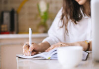 Close up of a woman writer hand writing in a notebook at home in the kitchen